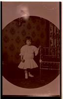 Retrato de Virgínia Maria Herman Pereira em criança junto a cadeira em casa.