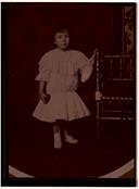Retrato de Virgínia Maria Herman Pereira em criança junto a cadeira em casa.