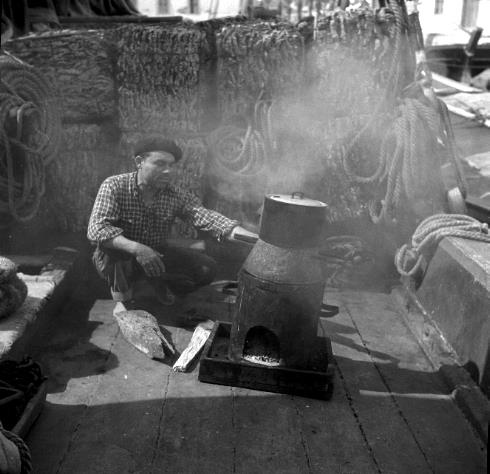 Legenda: Cozinhando num fogareiro a borda de uma embarca&ccedil;&atilde;o de transporte de corti&ccedil;a, d&eacute;cada de 1950.